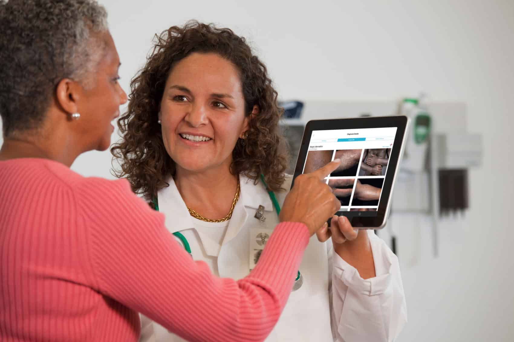 A doctor and a patient of color looking at VisualDx's dark skin dermatology atlas on a tablet